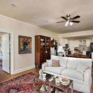 A cozy living room with a white sofa, colorful rug, artwork on the wall, and an open view of the kitchen.