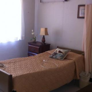 A simple bedroom with a single bed, lamp, and nightstand near a window.