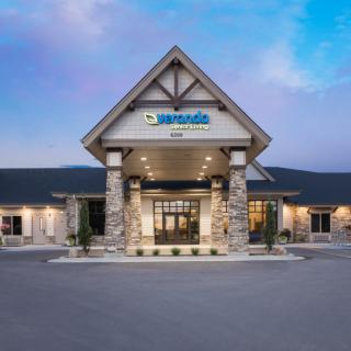 The exterior entrance of a commercial building with a peaked roof and stone columns against a clear sky.