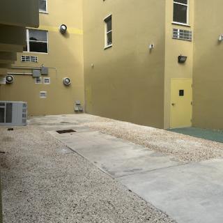 A view of a courtyard featuring yellow walls, paved surfaces, and air conditioning units in an urban setting.