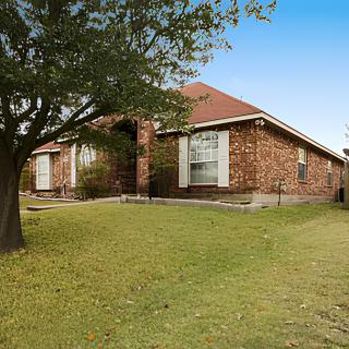 A suburban brick house with a spacious front yard and a tree.