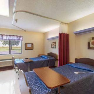 A hospital room with twin beds separated by a curtain, featuring a window and wall decorations.