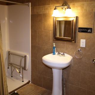 A well-lit bathroom with a pedestal sink, mirror, and accessible shower with handrails.