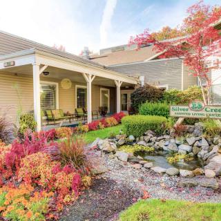 A beautiful house with a porch overlooking a well-maintained garden and pond, surrounded by vibrant autumn foliage.