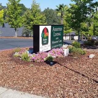 A well-maintained landscape featuring a business sign surrounded by greenery and flowers near a parking area.