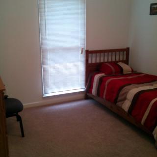 A minimalist bedroom with a single bed featuring striped bedding, a window with blinds, and a desk chair.