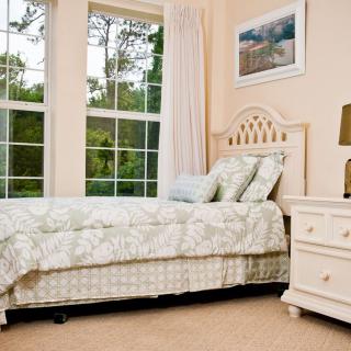 A cozy bedroom with a neatly made bed, soft lighting, and a large window overlooking greenery.