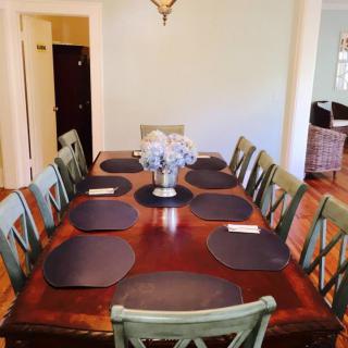 A spacious dining room with a large wooden table set with placemats and surrounded by chairs.