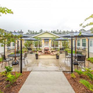 A well-maintained garden with outdoor seating and a central pathway, surrounded by greenery and lamp posts.