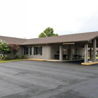 An exterior view of a small motel with a parking lot in front.