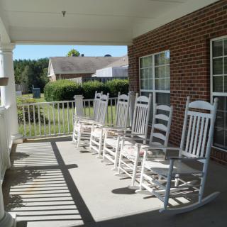 A sunny porch featuring a row of white rocking chairs, perfect for relaxation.