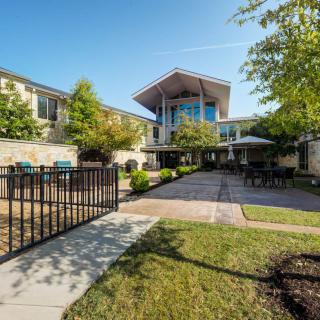 A modern building with a garden and pathway, surrounded by trees under a clear blue sky.