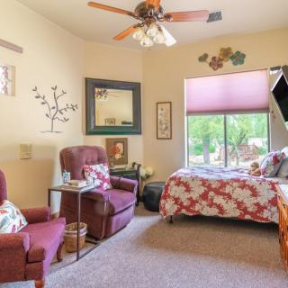 A cozy bedroom with comfortable armchairs and a floral patterned bed, featuring a large window that lets in natural light.