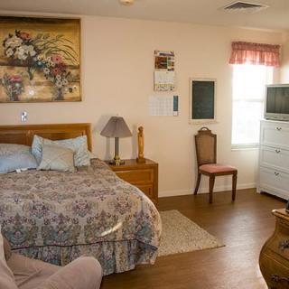 A cozy bedroom with a double bed, dresser, chair, and television.