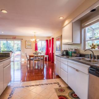 A modern kitchen and dining area with white cabinets and wooden flooring, illuminated by natural light.