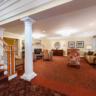 A spacious and elegantly decorated living room with a central column, comfortable seating, and a carpeted floor.