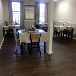 A dining area with several tables covered in white tablecloths, surrounded by chairs.