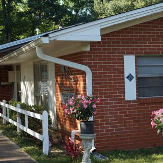 A brick house with a white fence and colorful flowers in the yard.