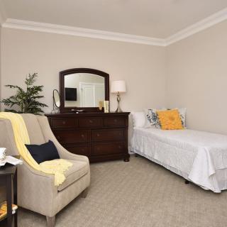 A cozy bedroom with a single bed, dresser, armchair, and decorative elements.