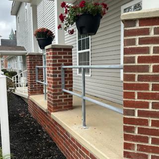 A well-maintained outdoor entrance featuring brick columns, railings, and hanging flower pots.