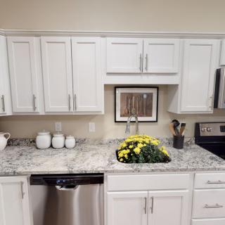 A modern kitchen with white cabinets, granite countertops, and stainless steel appliances.