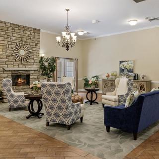A cozy living room featuring a stone fireplace, elegant chandelier, and comfortable seating arranged around a central coffee table.
