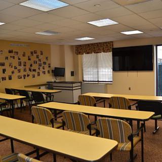 An empty classroom with desks, chairs, and a TV on the wall.