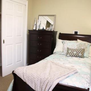 A cozy bedroom with a neatly made bed and a dresser topped with a mirror and decor items.