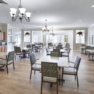 A spacious and elegantly designed dining area with multiple tables and chairs, featuring chandeliers and a wooden floor.
