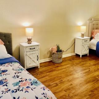 A cozy bedroom featuring two beds with floral bedding, complemented by nightstands and lamps on a hardwood floor.
