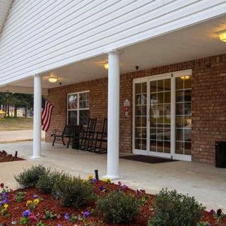 A welcoming building entrance with a porch featuring columns, a brick facade, and neatly arranged landscaping.