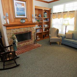 A cozy living room with a fireplace, armchair, and sofa, complemented by bookshelves and large windows.