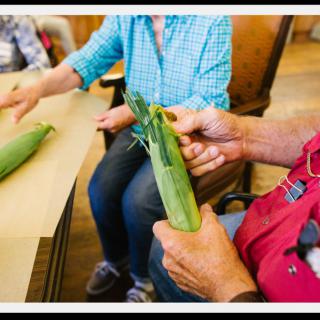 People sitting at a table, preparing corn.