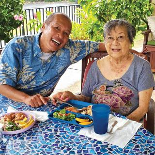 A cheerful moment shared by two people enjoying a meal outdoors in a tropical setting.