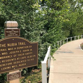 A sign marks the beginning of a nature trail, surrounded by lush greenery.