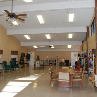 A spacious lobby area with tables, chairs, and ceiling fans under fluorescent lighting.