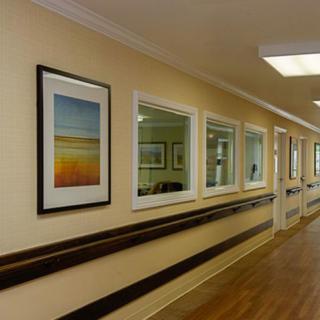 A well-lit hallway in a healthcare facility, featuring framed artwork and several windows.