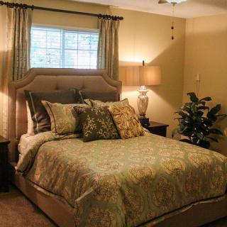 A cozy bedroom with elegant decor, featuring a large bed with multiple pillows, a window with curtains, and a lamp providing soft lighting.