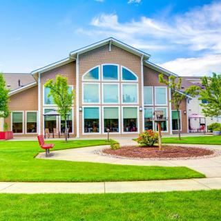 A modern building with large windows and a well-maintained lawn surrounded by trees and pathways on a clear day.