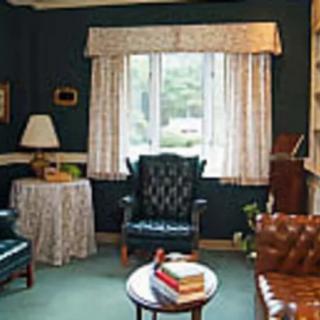 A cozy living room with traditional decor, featuring armchairs and a window with curtains.
