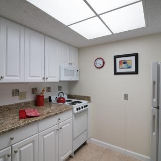 A small kitchen with white cabinets, granite countertops, and a compact stove, illuminated by overhead lighting.