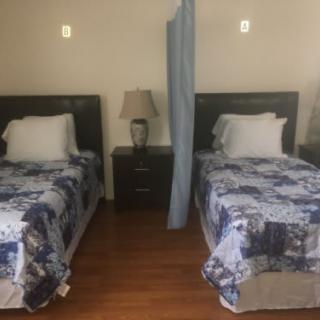 A cozy bedroom with two single beds separated by a curtain, featuring matching duvets and a bedside lamp.