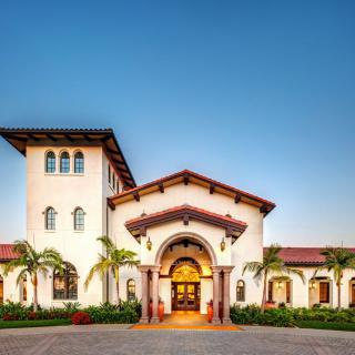 A Spanish-style building with an arched entrance, surrounded by palm trees, captured at sunset.
