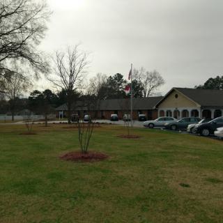 A view of a building with a flag in front, surrounded by grass and trees on a cloudy day.