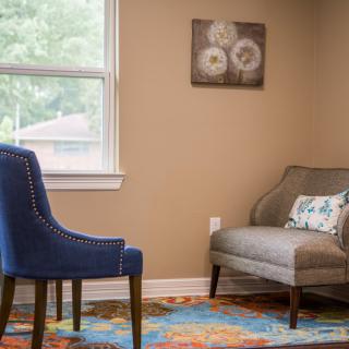 A cozy living room corner with a blue chair, gray sofa, and colorful rug.