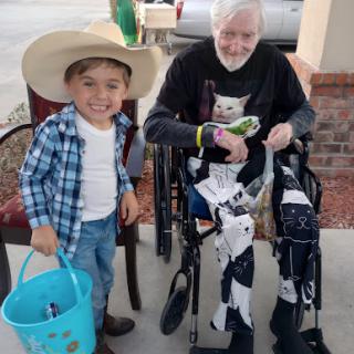 A young boy in a cowboy hat shares a joyful moment with an elderly man, both smiling and enjoying their time together.
