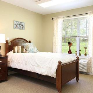 A cozy bedroom with a wooden bed, bedside table, and ample natural light from a large window.