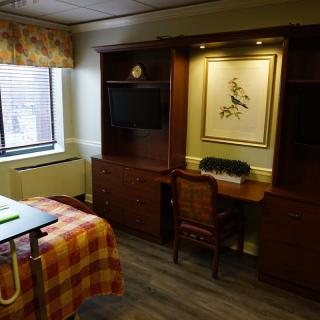 A cozy bedroom with a desk and chair, featuring a window and artwork on the wall.