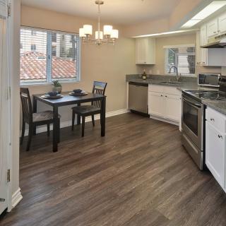 A modern kitchen with hardwood floors, stainless steel appliances, and a small dining area by a large window.