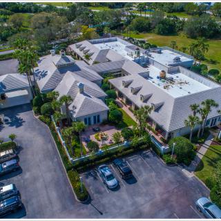 Aerial view of a complex with multiple buildings surrounded by greenery and a parking lot.